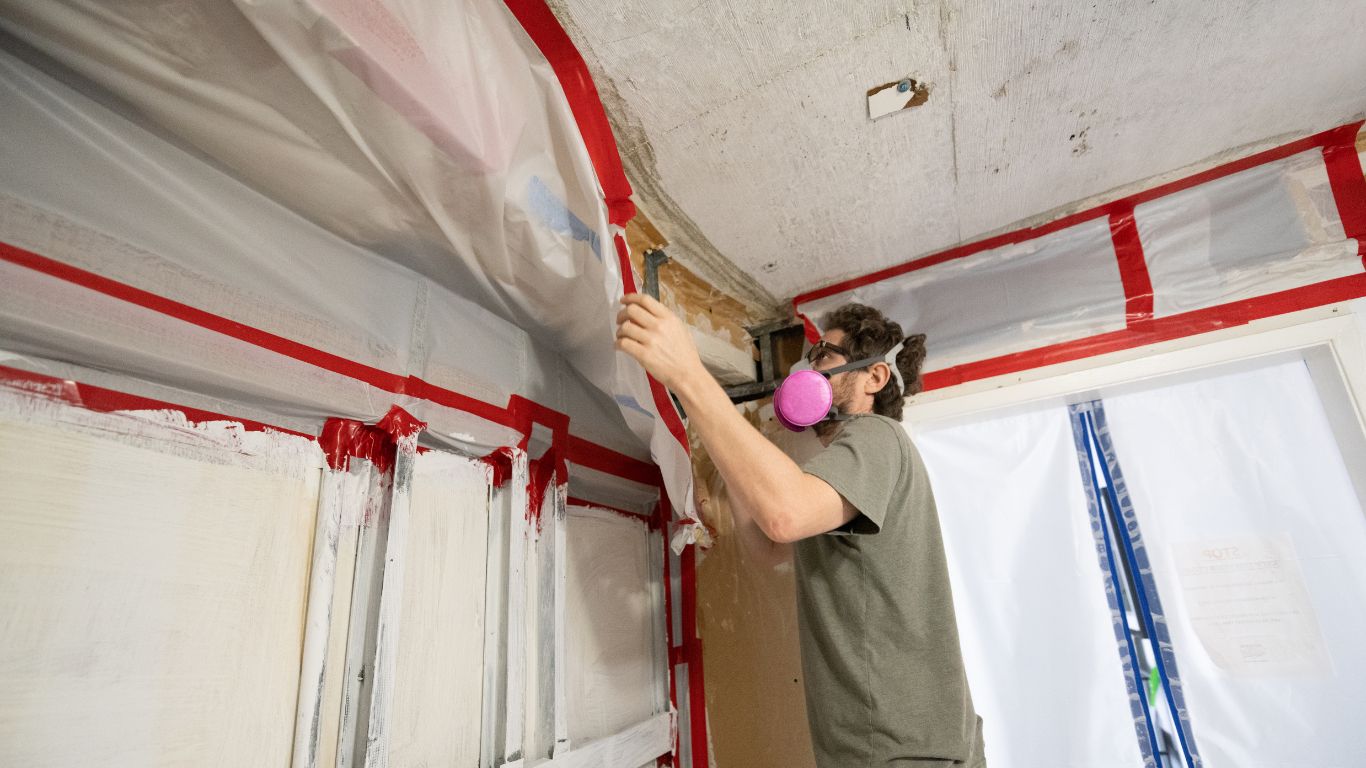 Professional performing mold remediation in Stamford, removing plastic covering from a wall.