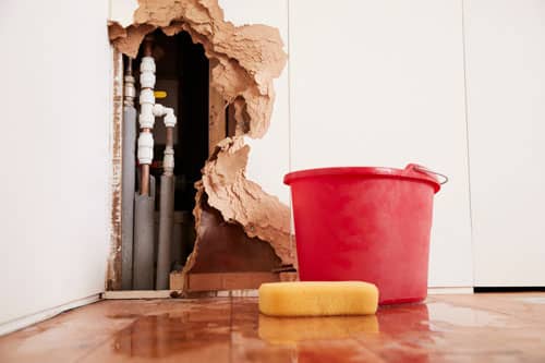 a hole in the wall caused by water damage with a red bucket