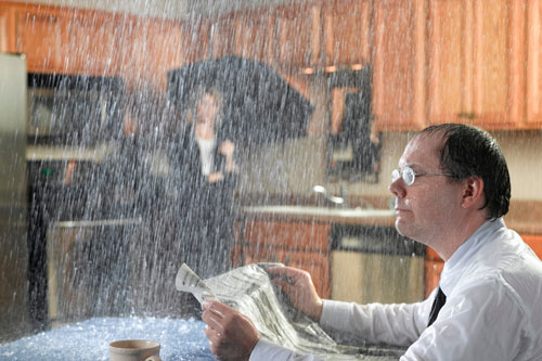 man sitting in kitchen reading paper while rain pours inside