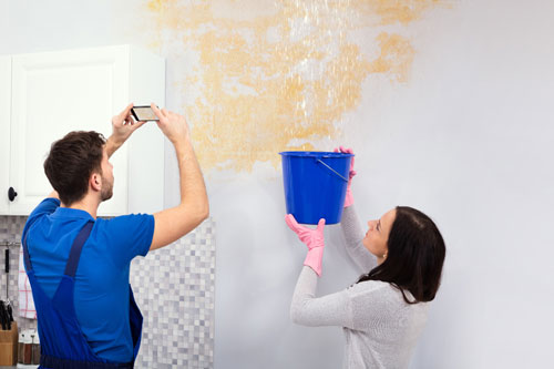 couple taking photos of water damage and catching water