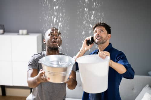 two men catching water with buckets in a house